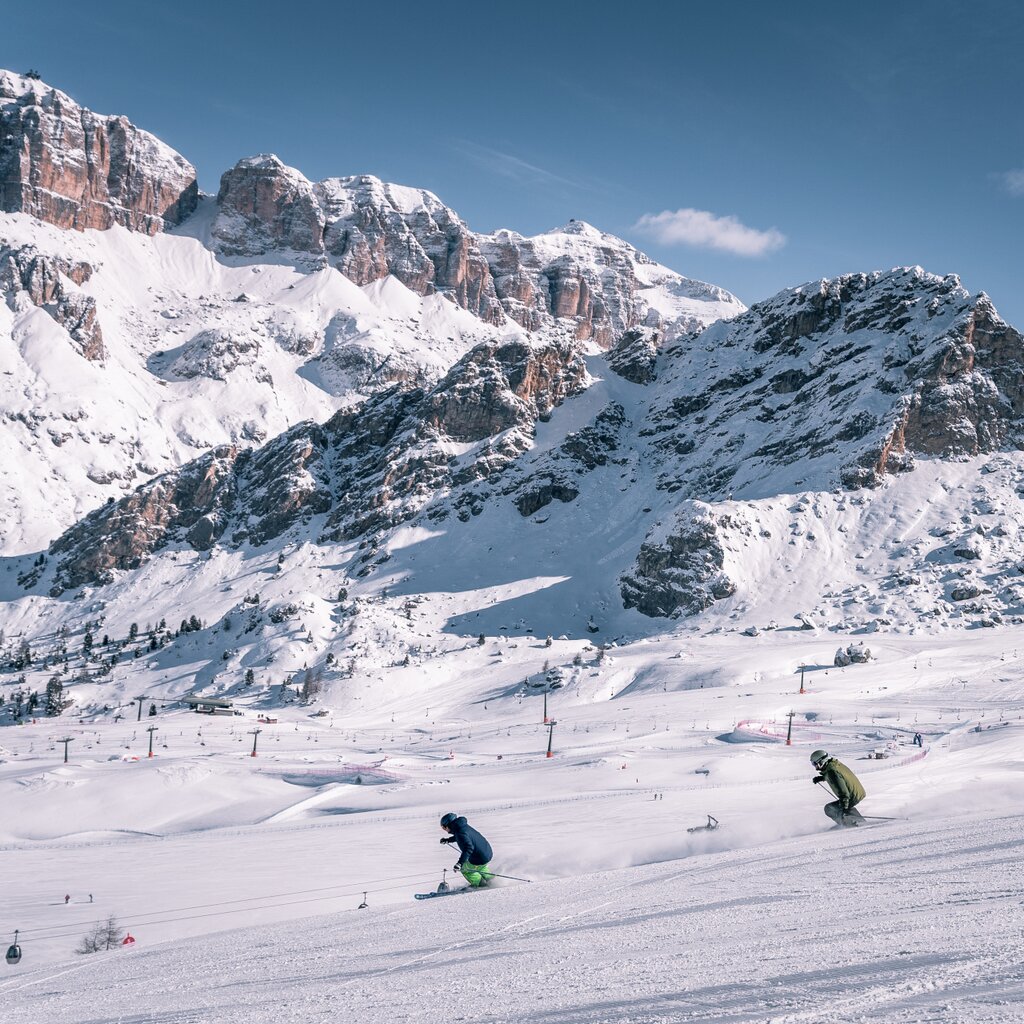 Coppia di amici scia sulle piste della skiarea Belvedere di Canazei. Sullo sfondo Sass Becé e Sass Pordoi | © Patricia Ramirez  - Archivio immagini ApT Val di Fassa