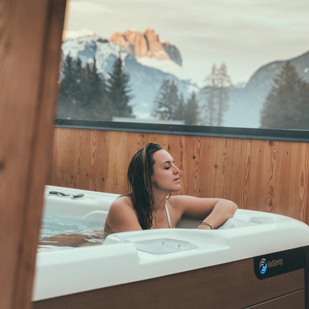 Persona nella vasca idromassaggio esterna con vista sulle Dolomiti innevate in Val di Fassa | © Federico Modica - Archivio Immagini ApT Val di Fassa