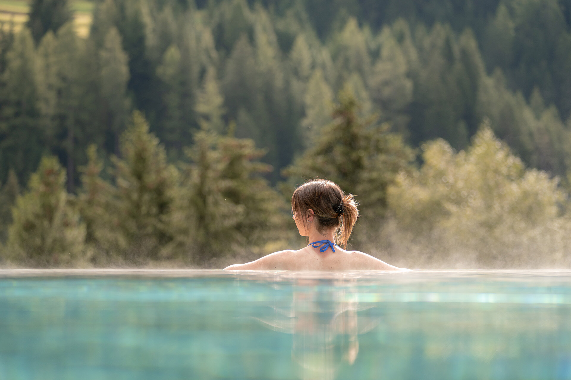 Ragazza di spalle in una piscina esterna con vista sulle Dolomiti in Val di Fassa | © Mattia Rizzi - Archivio Immagini ApT Val di Fassa 